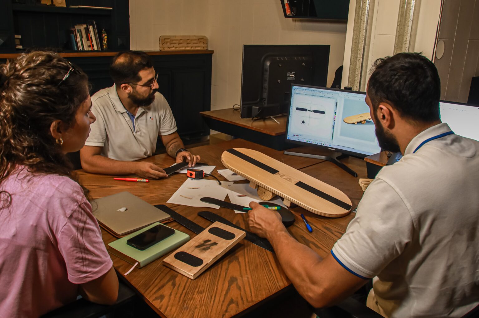 Ali Haidar and the HAI team reviewing a wooden balance board prototype and its design on screen